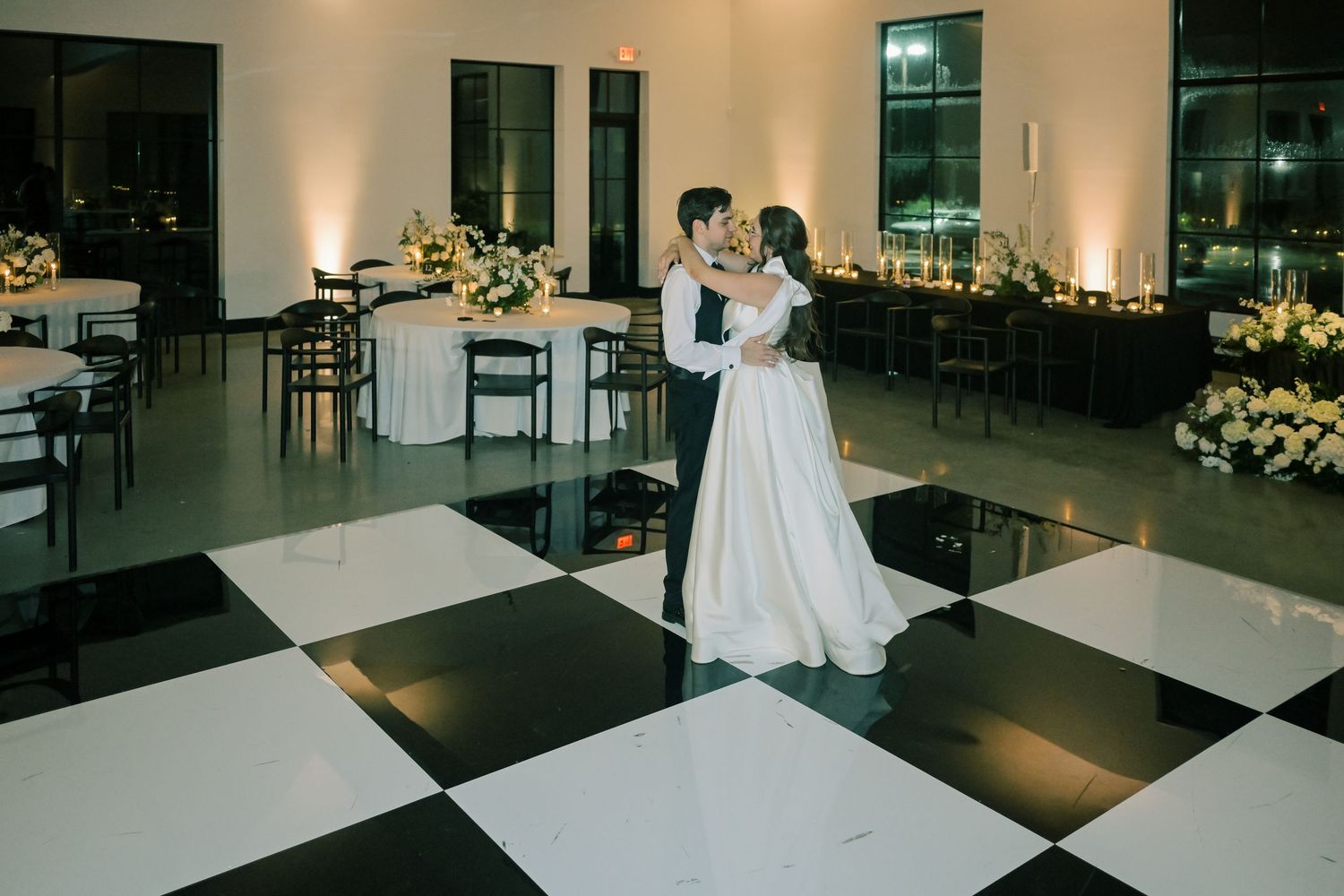 Bride and groom share their first dance on a black and white checkered dance floor.