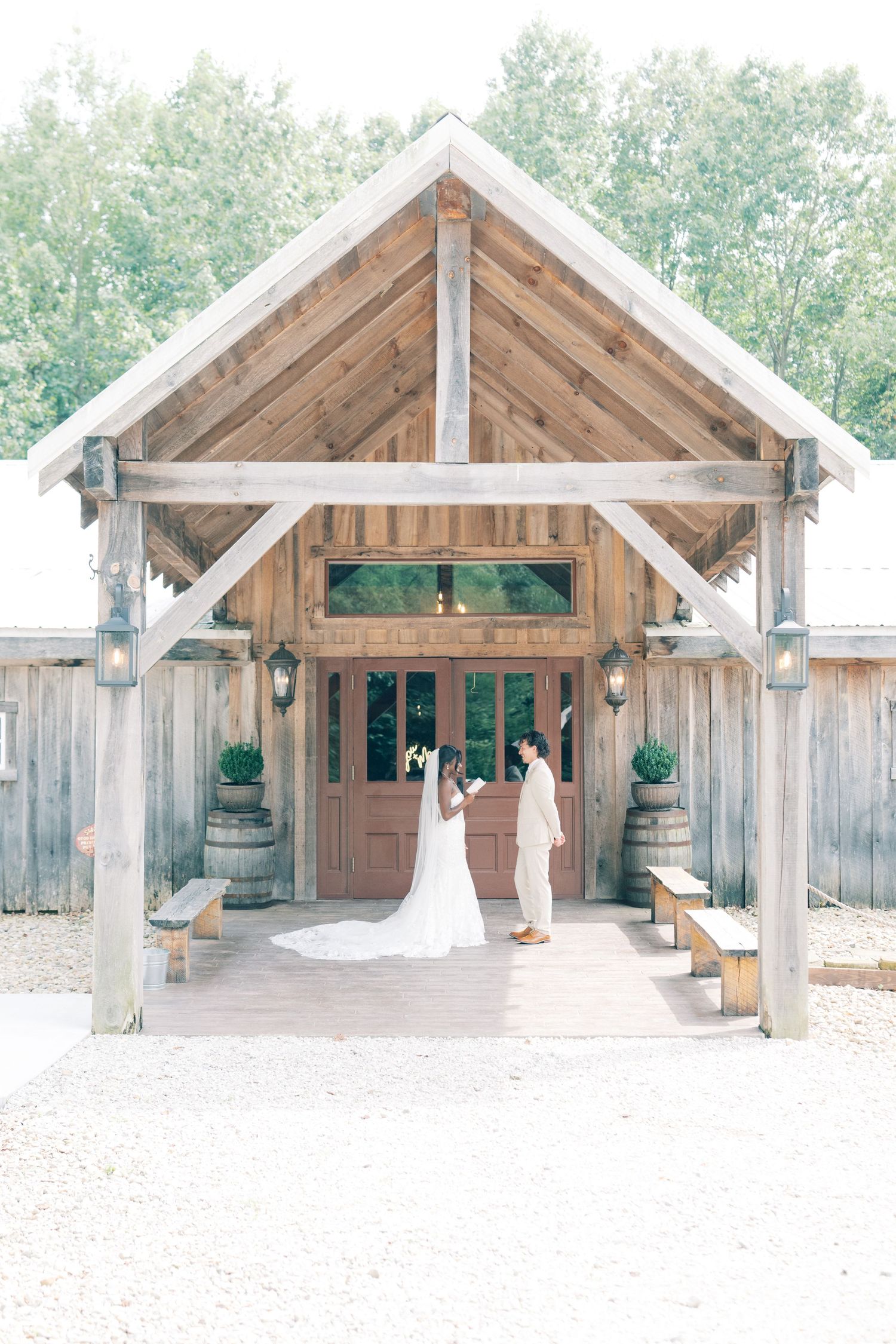 Bride and groom share a romantic moment at the entrance of a rustic wooden barn wedding venue.
