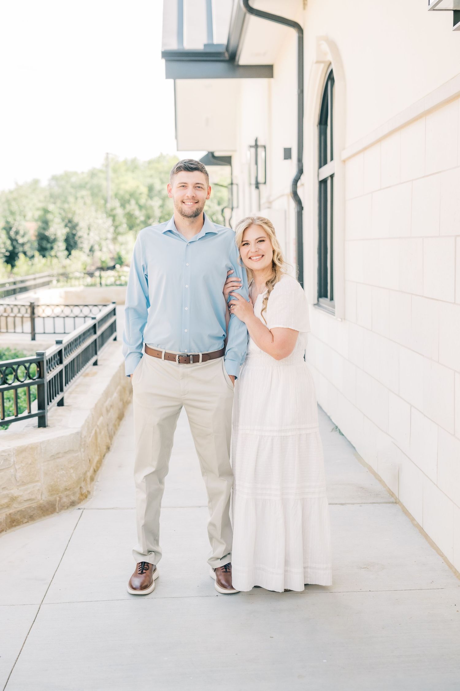 Smiling couple posing together on a sunlit outdoor walkway, dressed in blue and white.