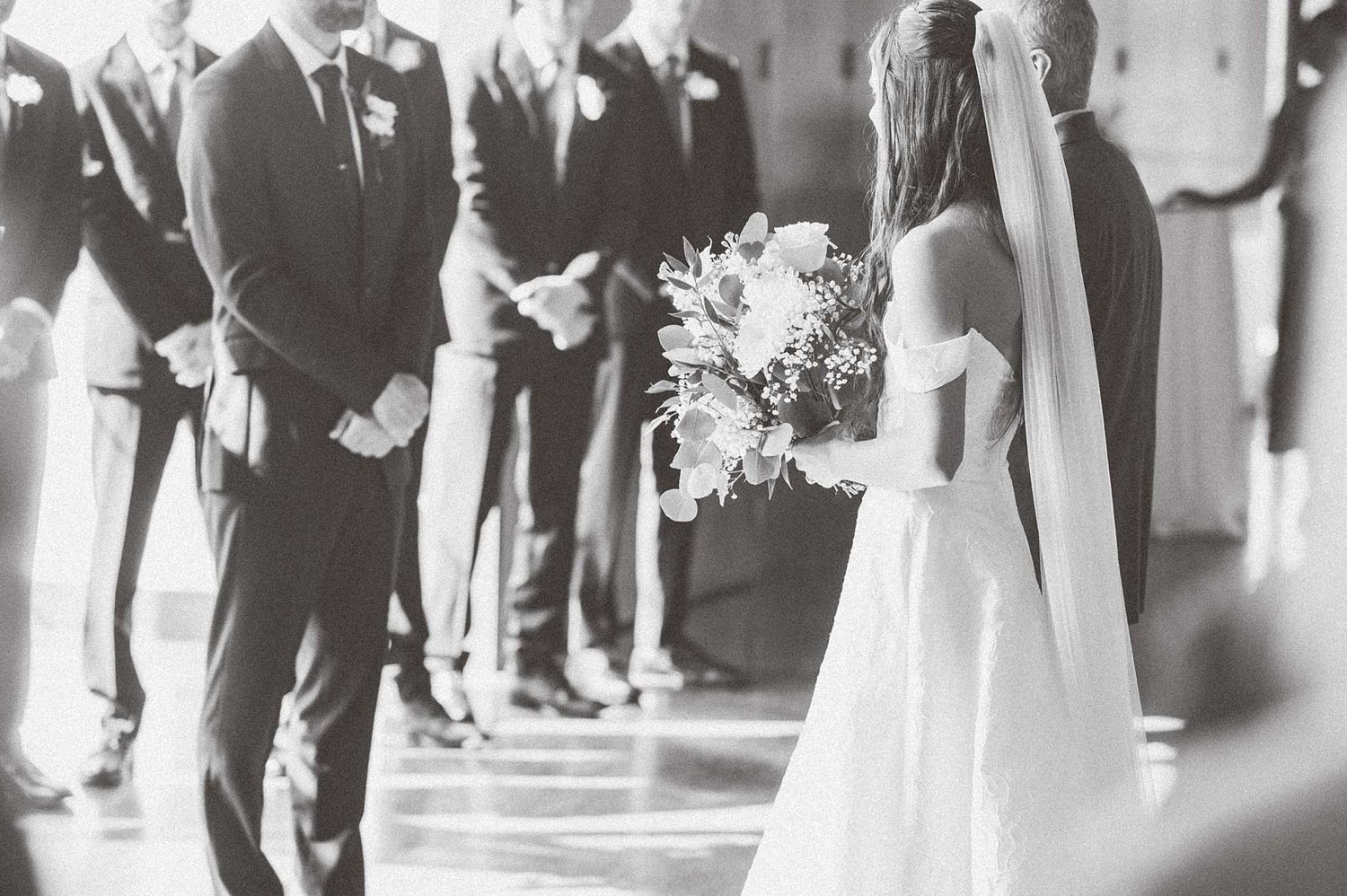 Wedding ceremony taking place in a bright indoor venue with guests seated in rows.
