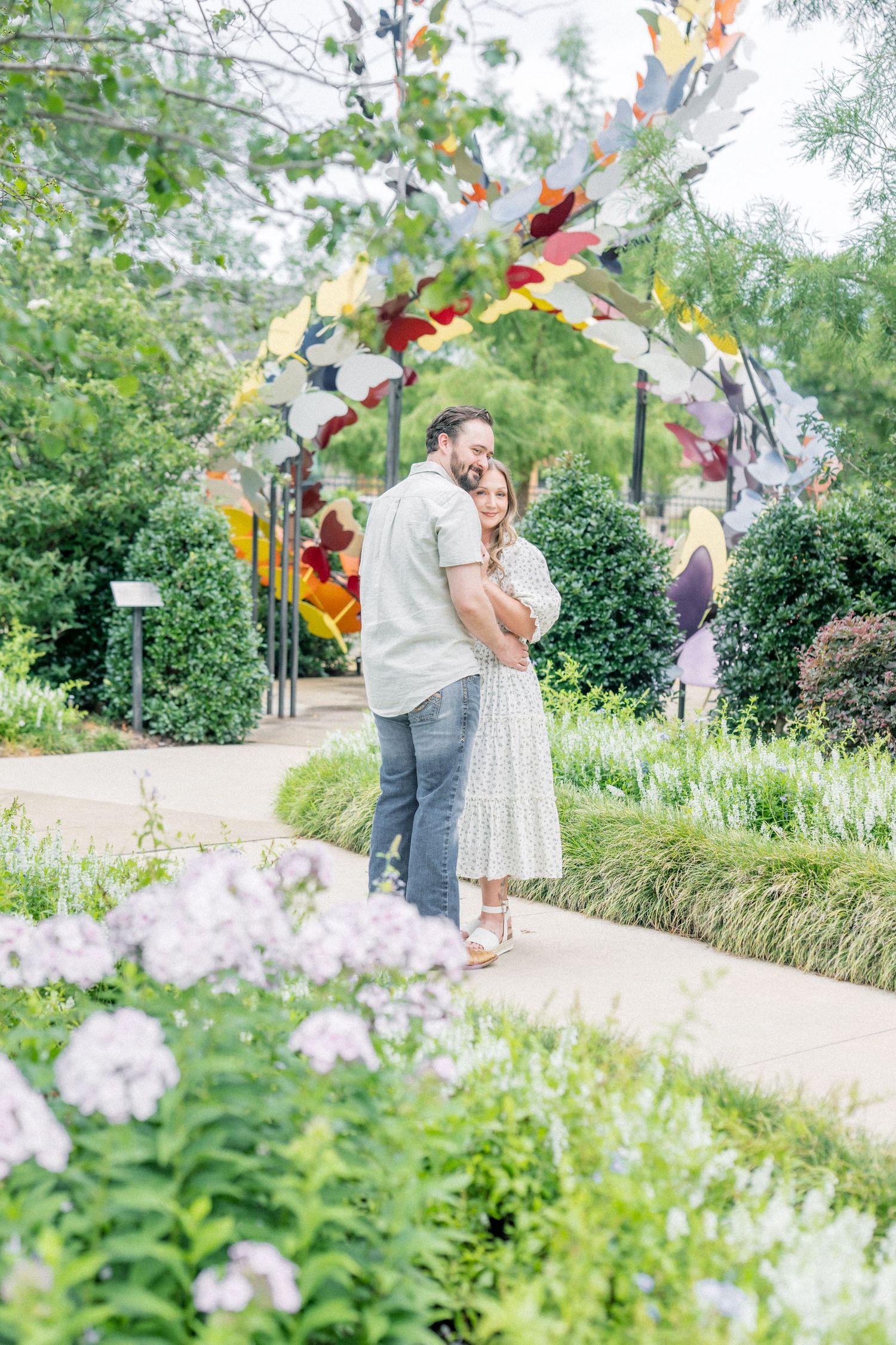 Couple hugging under a colorful butterfly arch in a lush botanical garden.