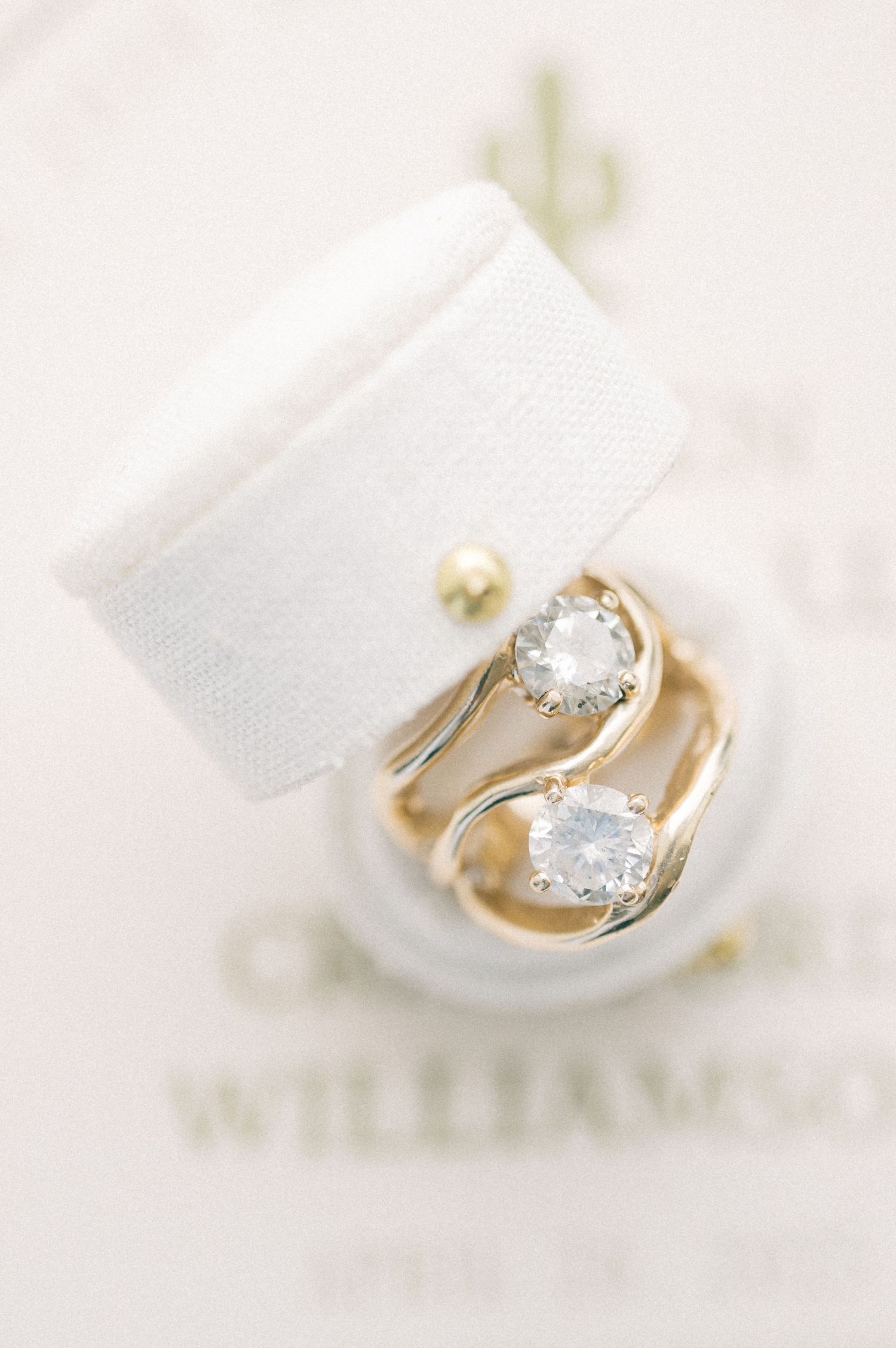 Gold two-stone diamond engagement ring and wedding band displayed in a white velvet ring box.
