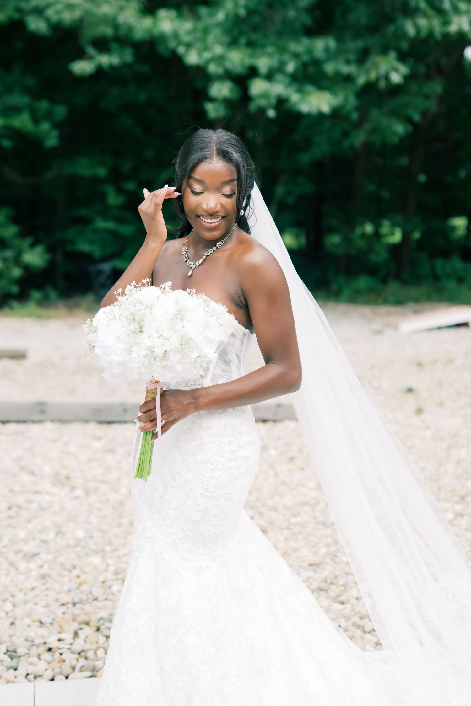 Elegant Black bride in strapless lace mermaid gown holds white hydrangea bouquet with flowing veil.