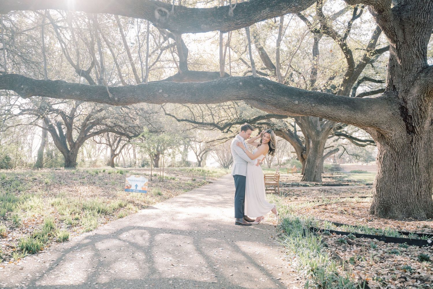 A couple stands together under a large tree branch in a scenic outdoor park setting during winter.