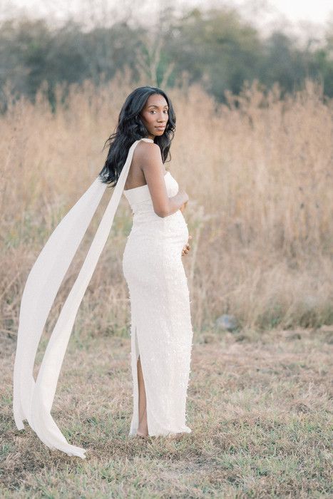 A flowing white dress catches the breeze in an outdoor photoshoot set against tall grass and natural scenery.