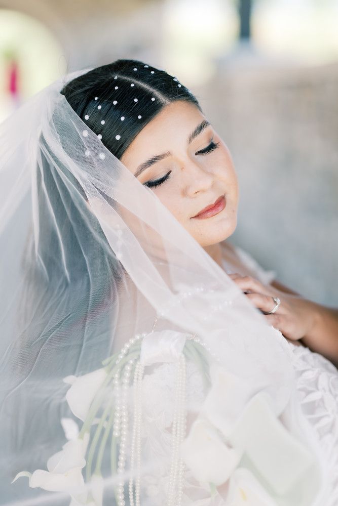 A bride in a delicate white veil and pearl accessories poses with closed eyes in a soft, ethereal bridal portrait series.