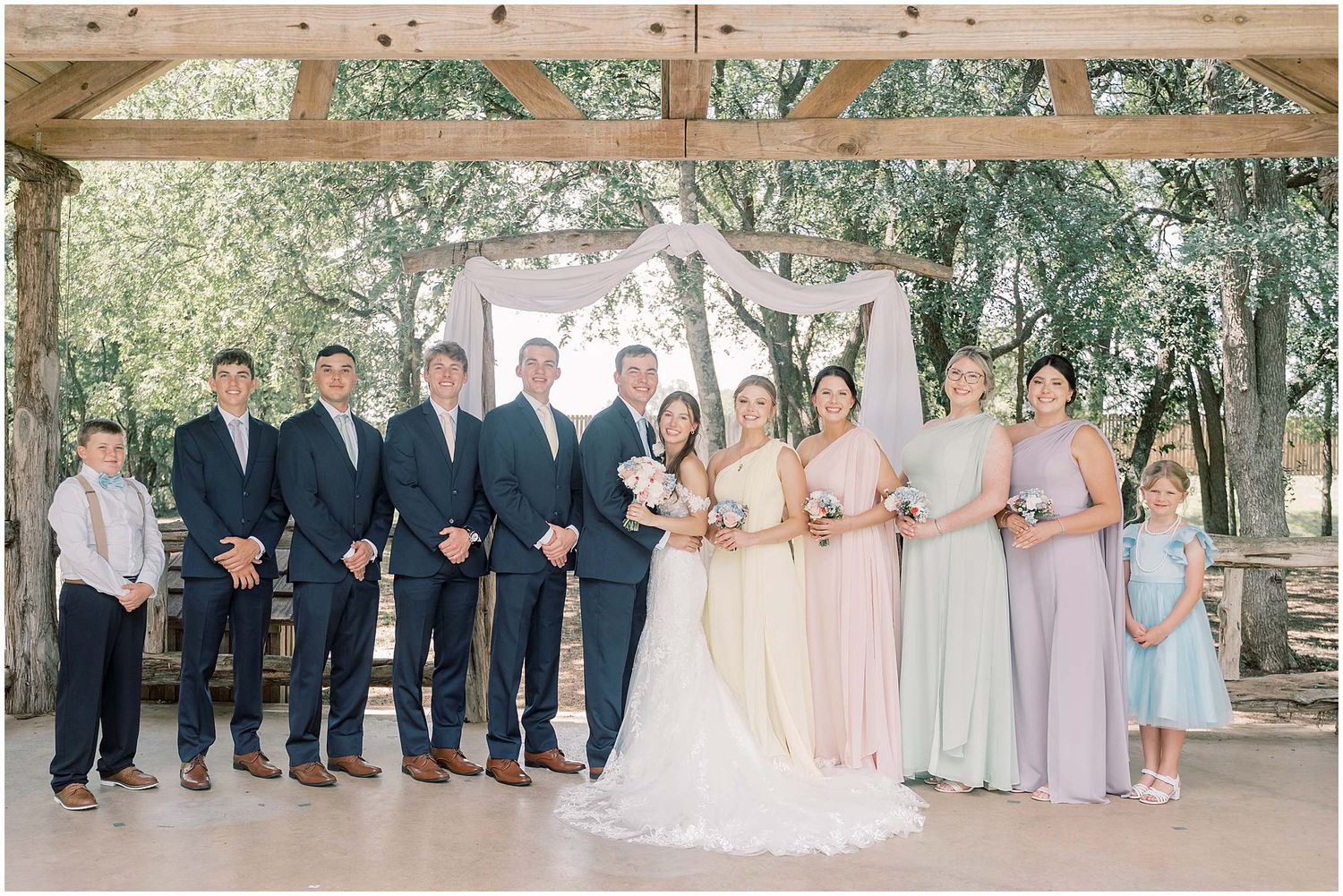 Wedding party members in pastel blue and pink dresses and navy suits pose together for formal outdoor portraits.