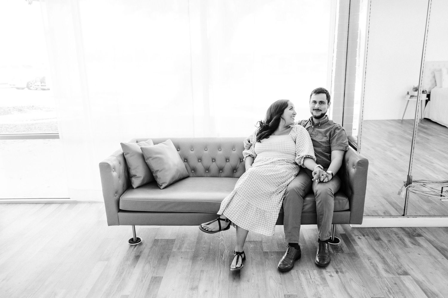 A candid black and white photo of a couple sitting together on a gray tufted sofa.