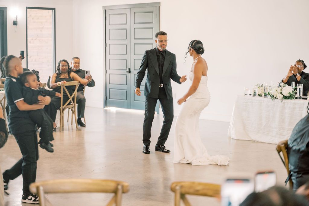 Bride and groom share their first dance at a modern wedding reception venue with guests celebrating around them.