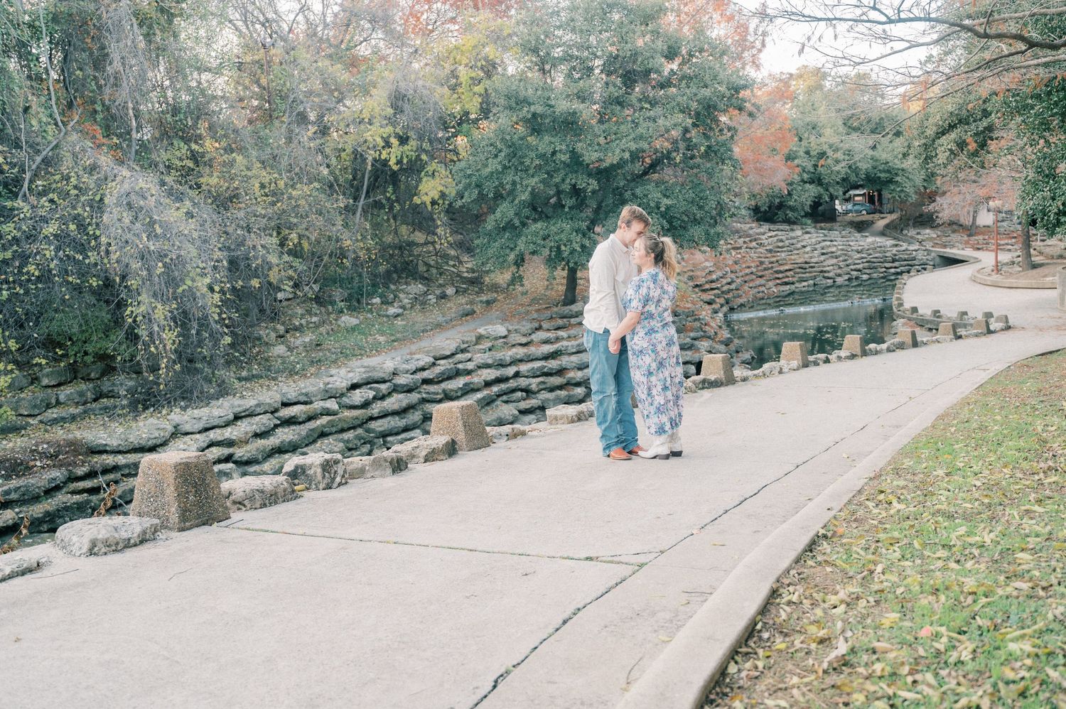 A couple walks along a scenic stone pathway through a garden during autumn with colorful foliage in the background.