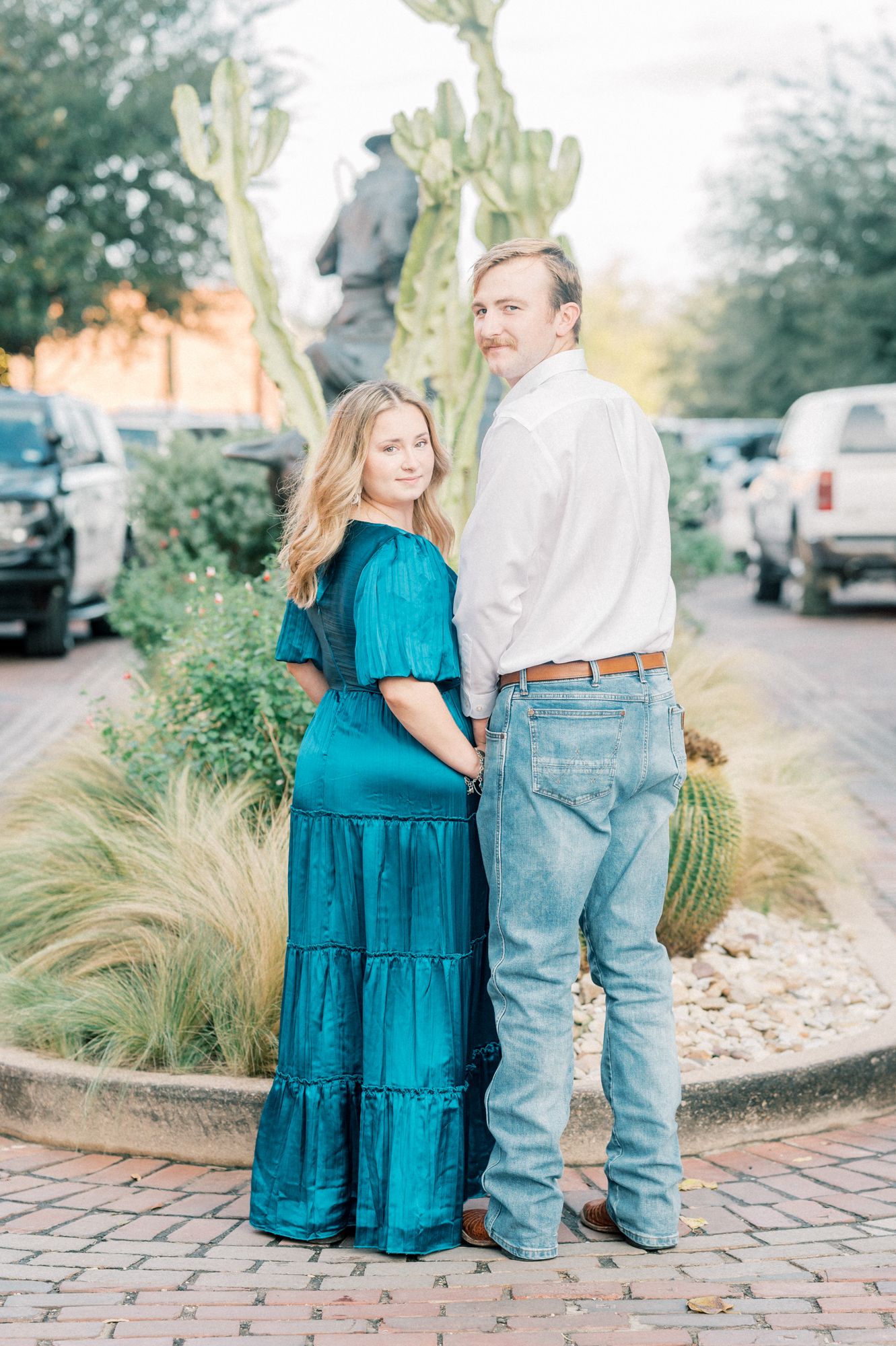A couple poses together on a brick path with desert landscaping and cacti in the background.