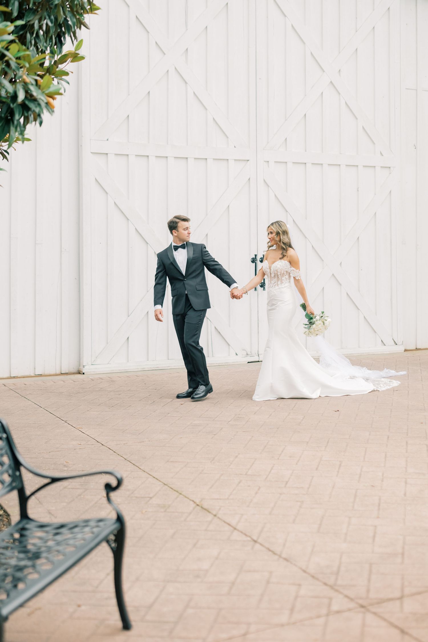Bride and groom holding hands in front of large white barn doors at an outdoor wedding venue.