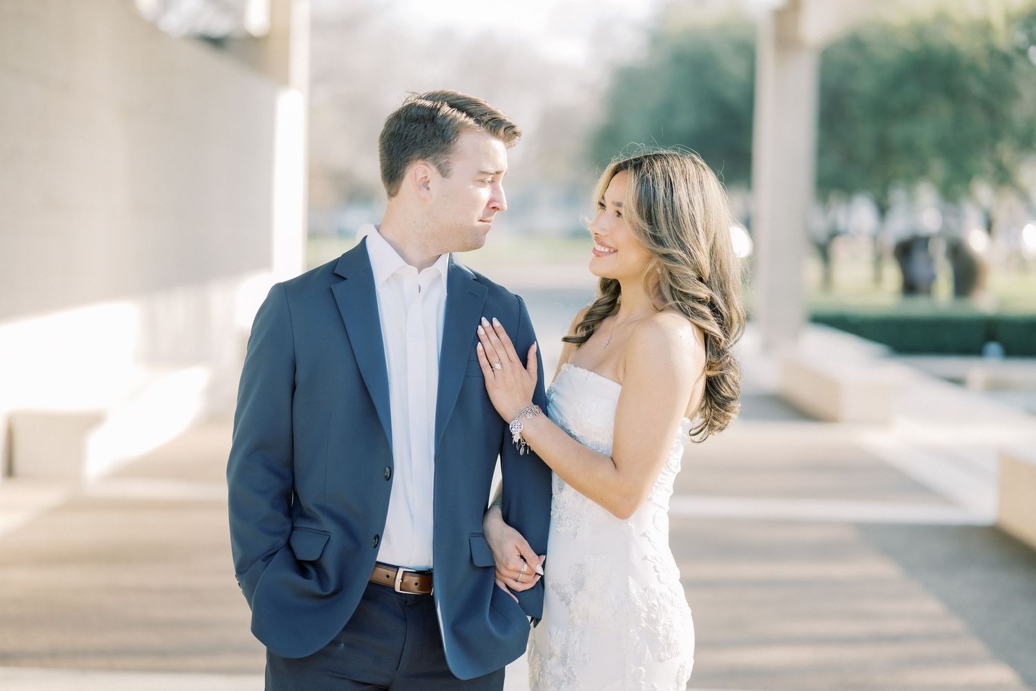 A couple in wedding attire shares an intimate moment while walking together outdoors on a bright sunny day.