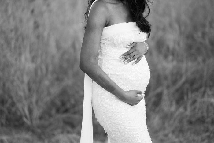 Elegant maternity photo in black and white showing a woman in a flowing white dress cradling her baby bump.