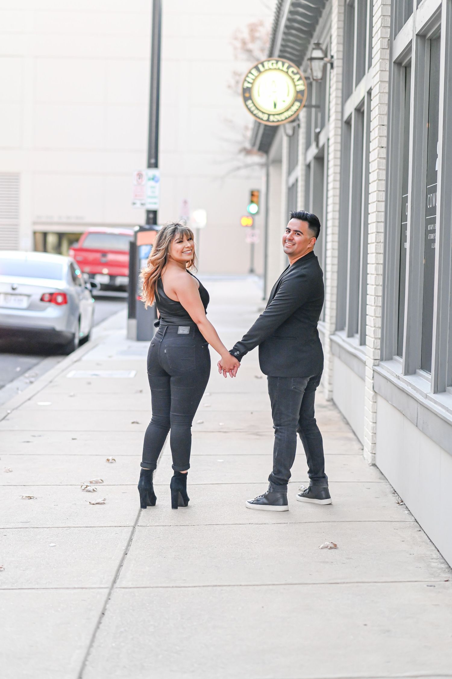 Couple holding hands on an urban sidewalk, both dressed in dark outfits with ankle boots.