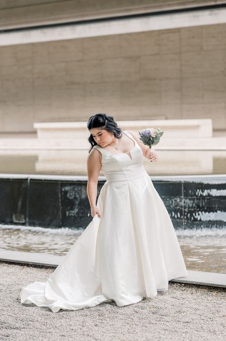 Bride in white ball gown holding bouquet near fountain.
