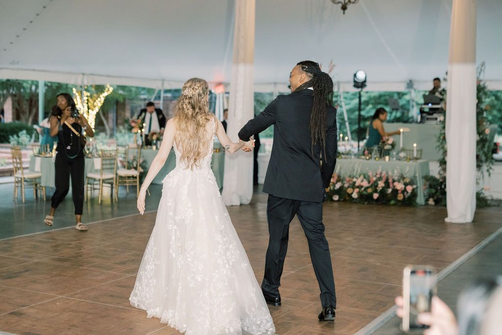 Bride and groom share their first dance under a white tent at an elegant wedding reception.