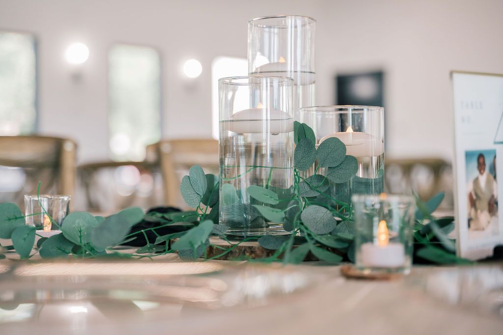 Elegant wedding table centerpiece with floating candles in glass cylinders and eucalyptus greenery garland.
