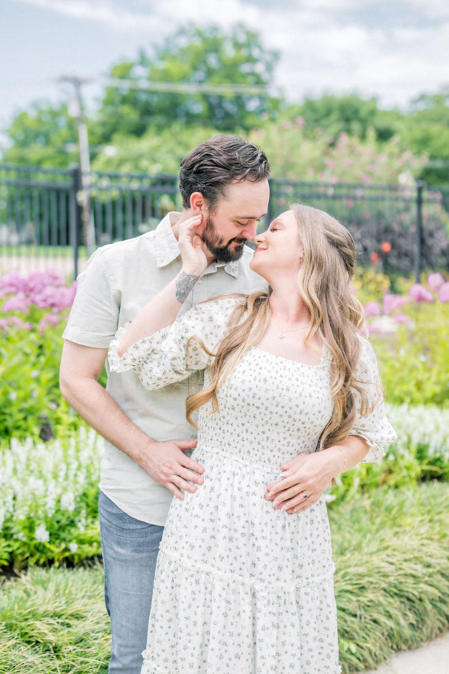 Couple sharing a romantic almost-kiss moment surrounded by vibrant garden flowers.