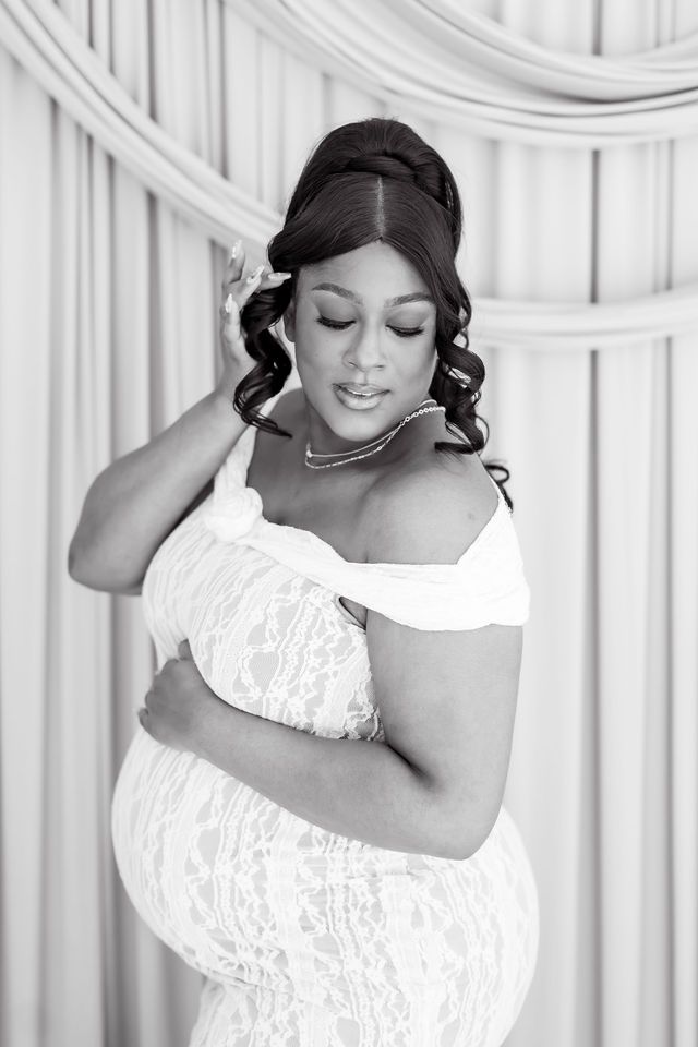 Black and white maternity photo of elegant pregnant woman in lace off-shoulder gown with updo hairstyle.