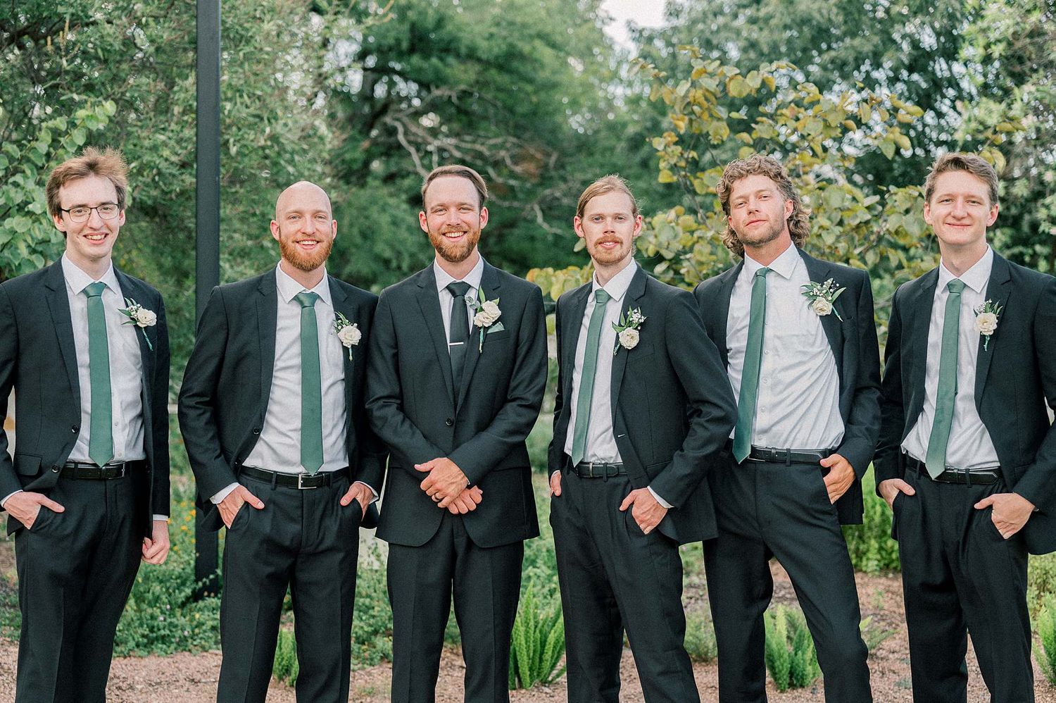 Groomsmen in black suits and mint green ties pose together outdoors.