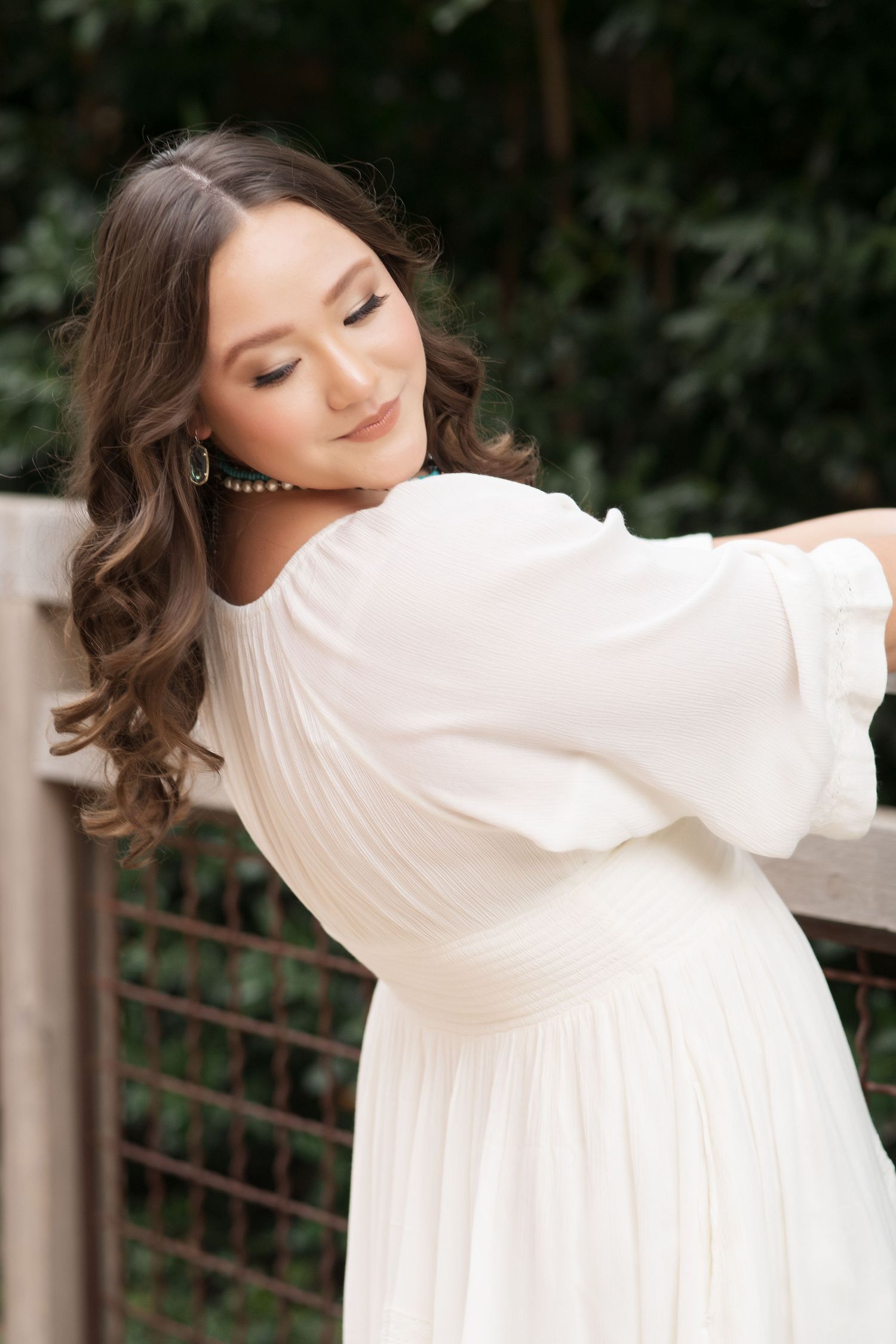 Woman in elegant white dress with flowing sleeves poses gracefully against outdoor railing.