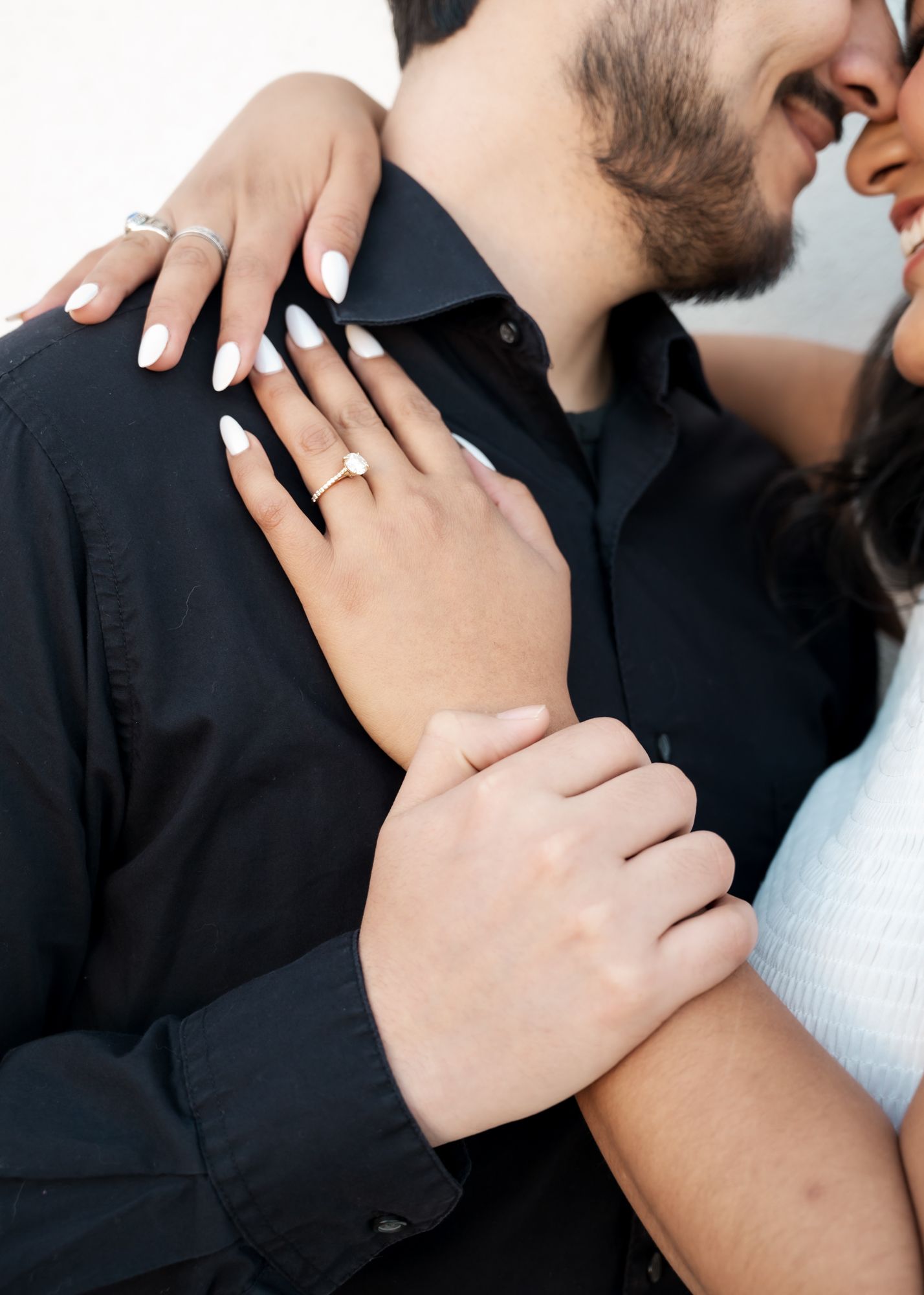 Close-up shot showing hands with engagement rings and intimate embrace.