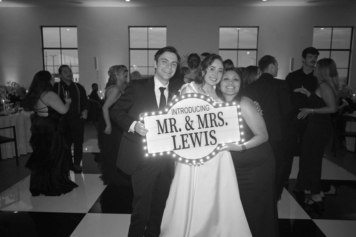 Newlyweds Mr. and Mrs. Lewis smiling and posing with an illuminated marquee sign at their wedding reception.