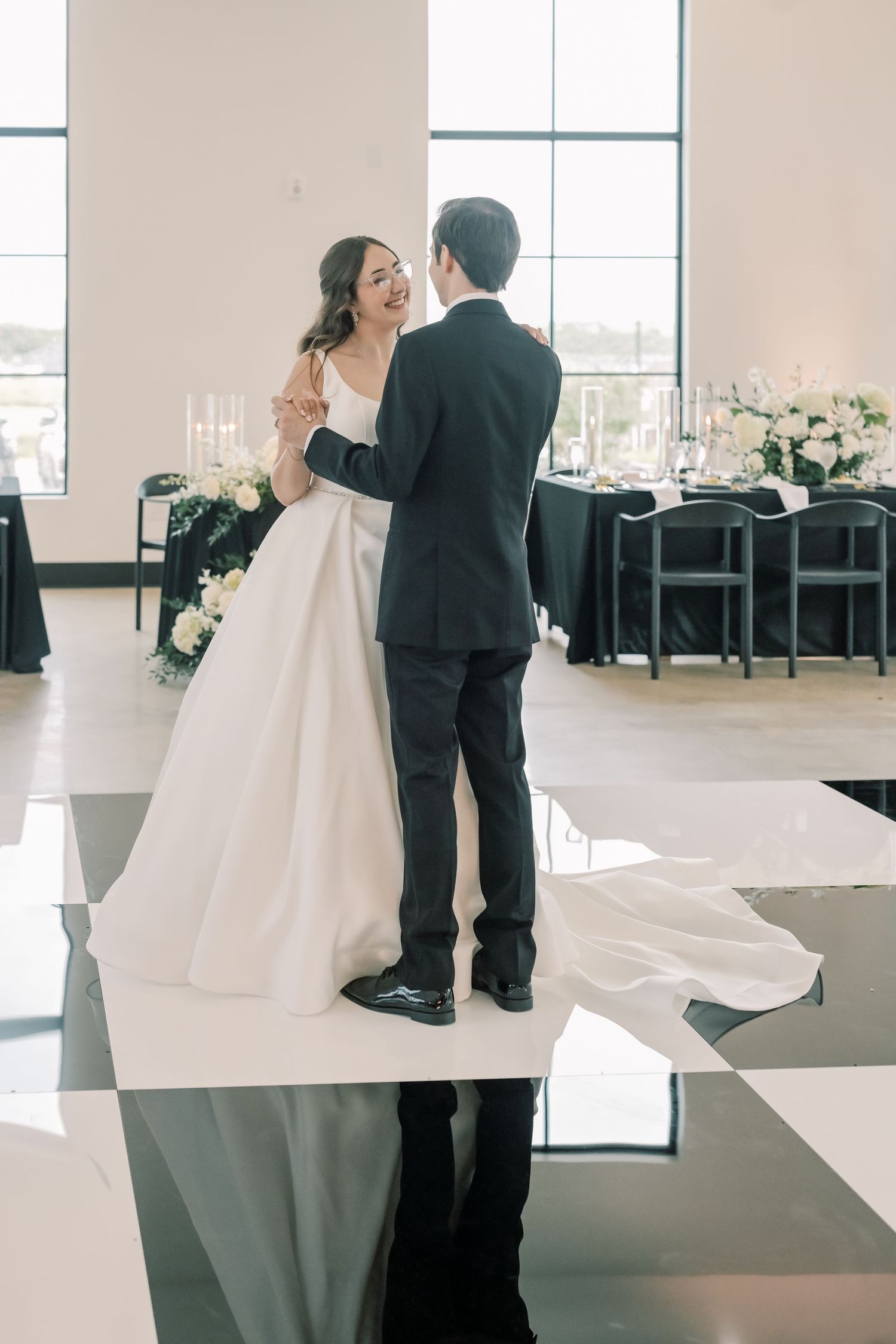 Bride and groom share first dance on black and white checkered floor at wedding reception.