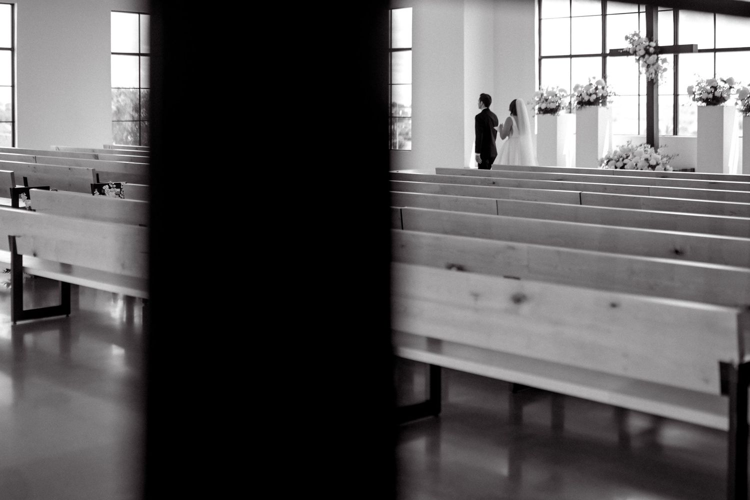 Black and white photo of bride and groom standing at the altar of a modern church.