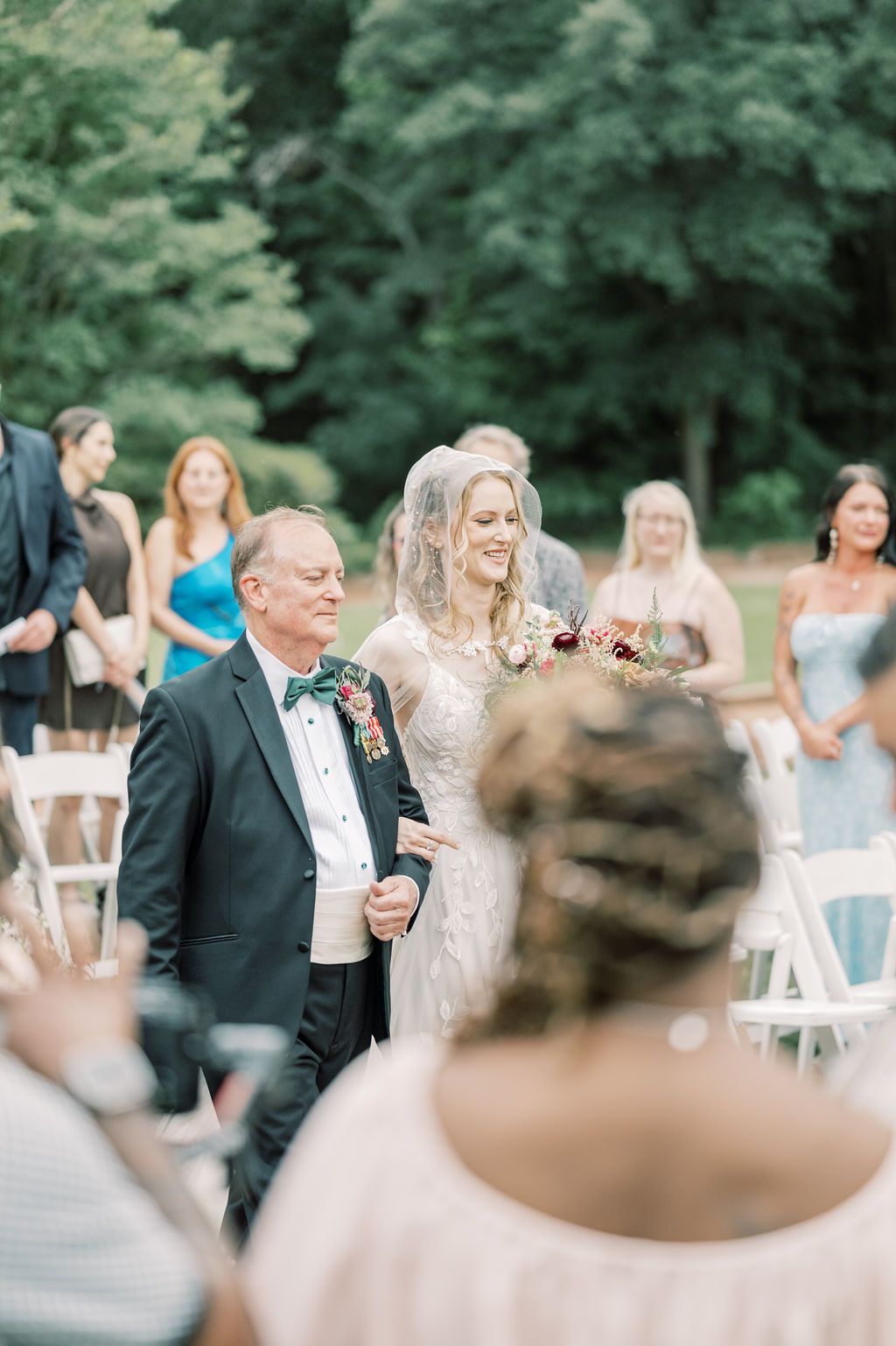 Bride walking down the aisle with her father at an outdoor wedding ceremony, smiling joyfully.