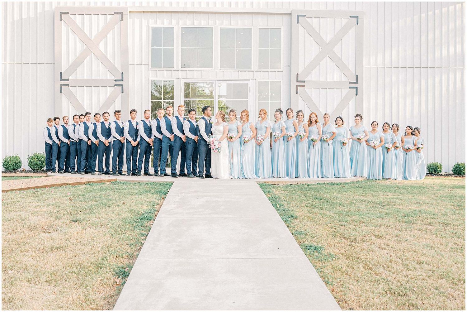 Wedding party members lined up outdoors in coordinating blue and pink attire for formal group photos.