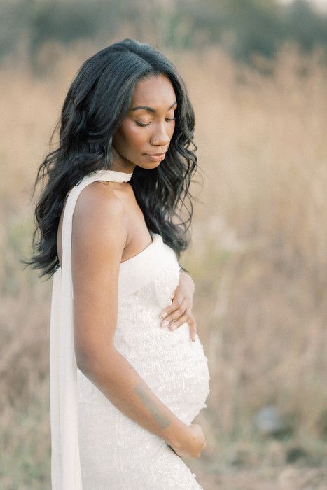 Elegant maternity portrait with flowing white dress against a natural outdoor backdrop.