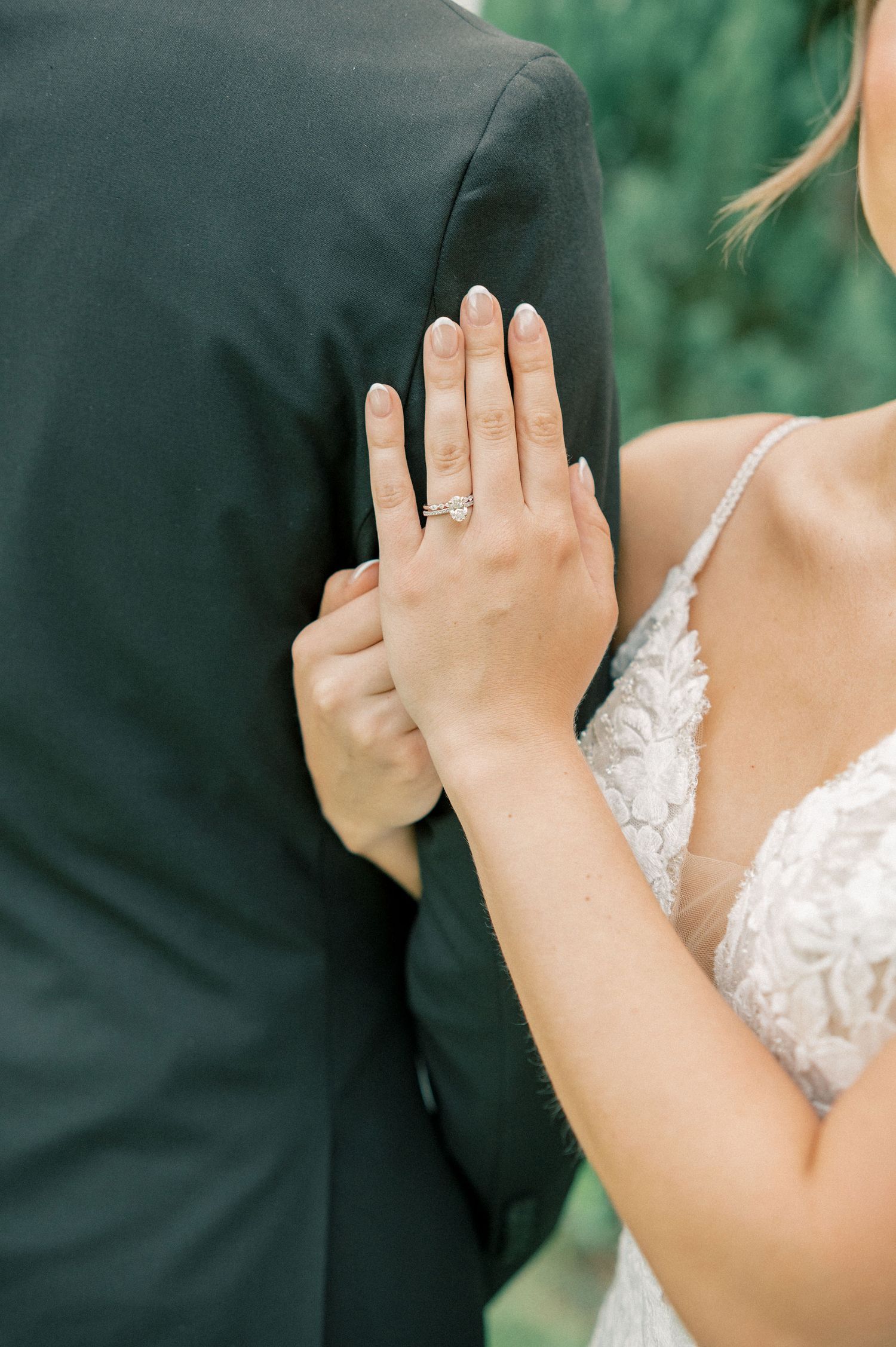 A close-up shot showing a hand with an engagement ring resting against a dark suit jacket.