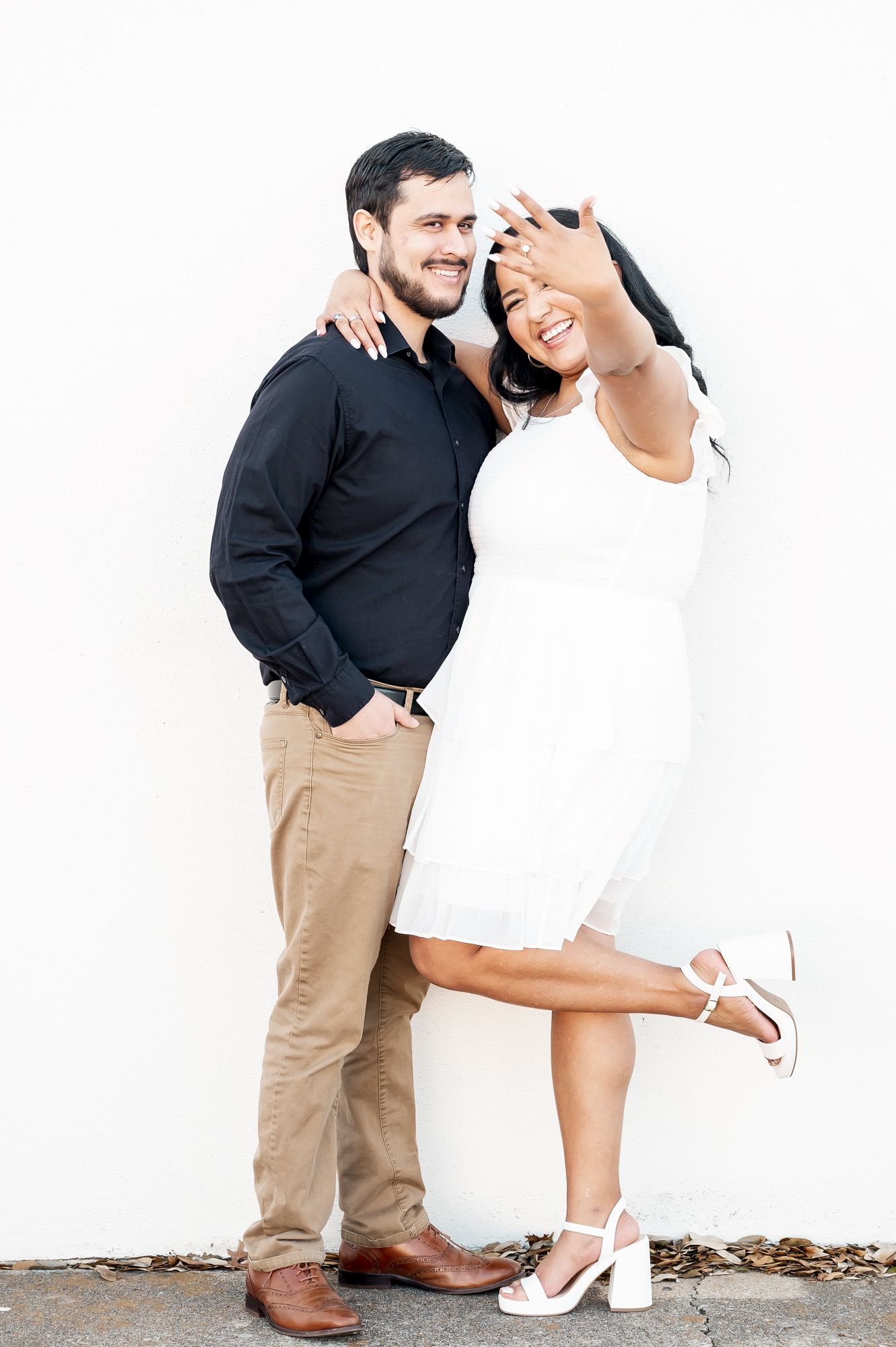 A couple in contrasting black and white outfits pose playfully against a white wall in a series of romantic shots.