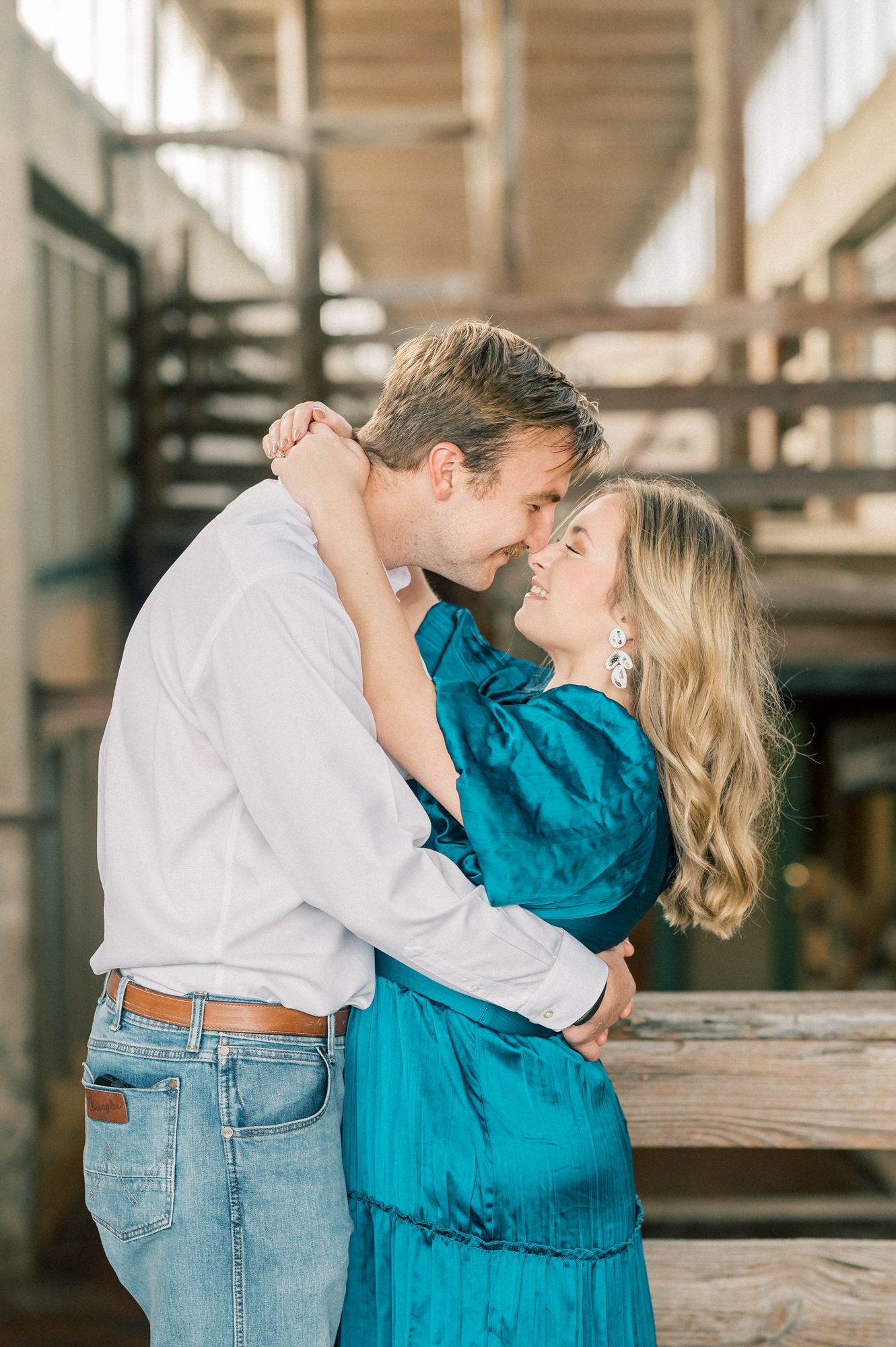 A romantic couple in teal and denim embrace and dance in a rustic indoor setting with natural light.