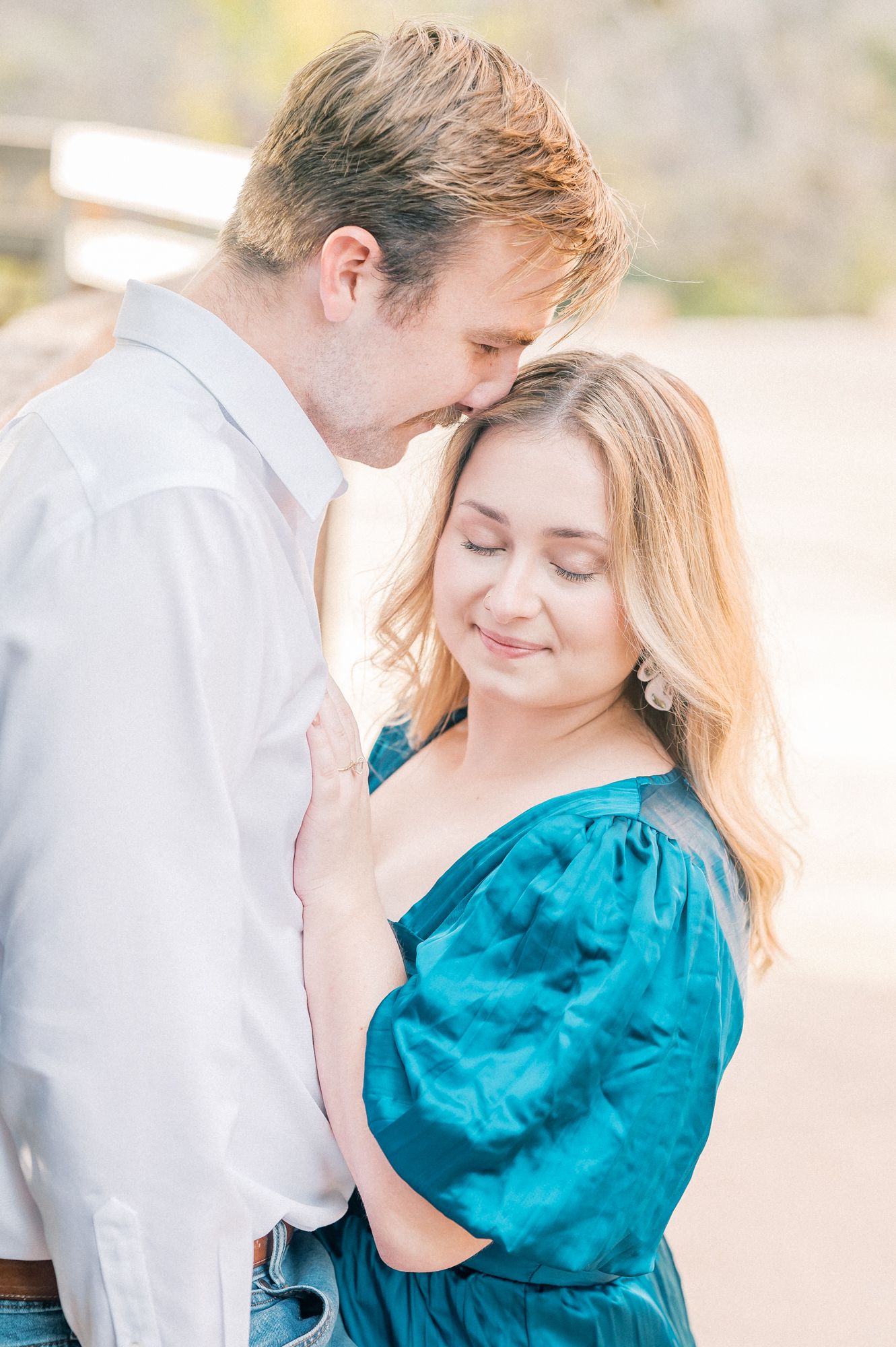 Couple shares romantic moment on bridge with woman in teal dress and man in white shirt.