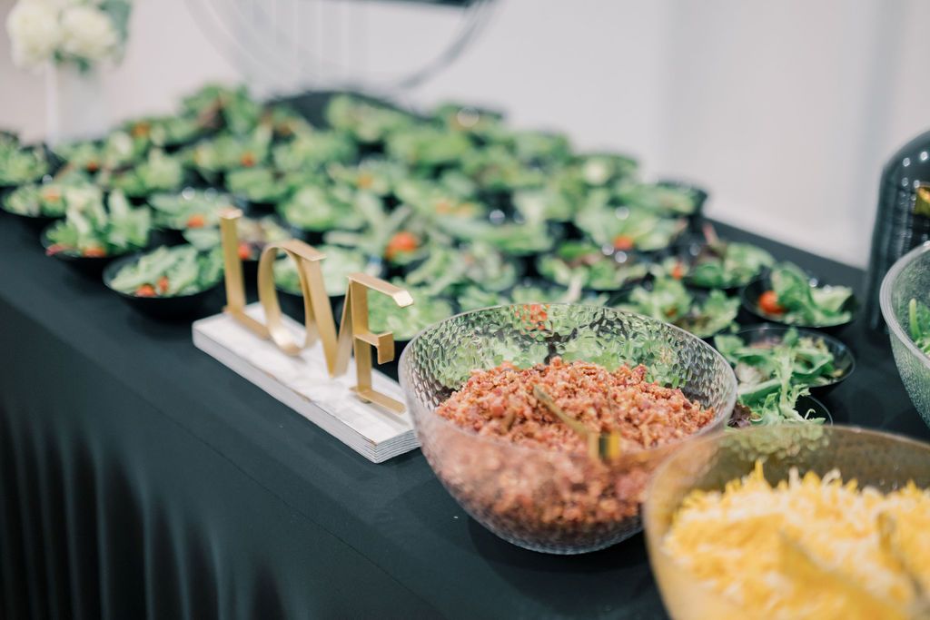 Elegant buffet table with fresh salads, grain bowls, and yellow rice displayed in glass bowls at a catered event.