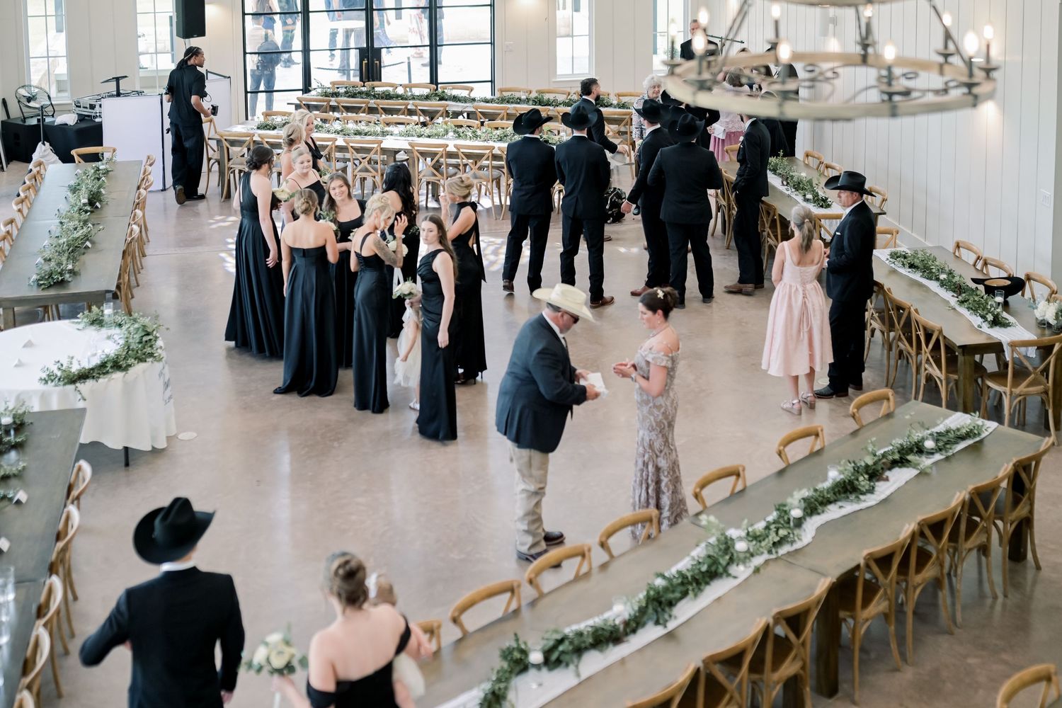 Aerial view of wedding reception hall with long tables, greenery garlands, and guests in black formal attire.