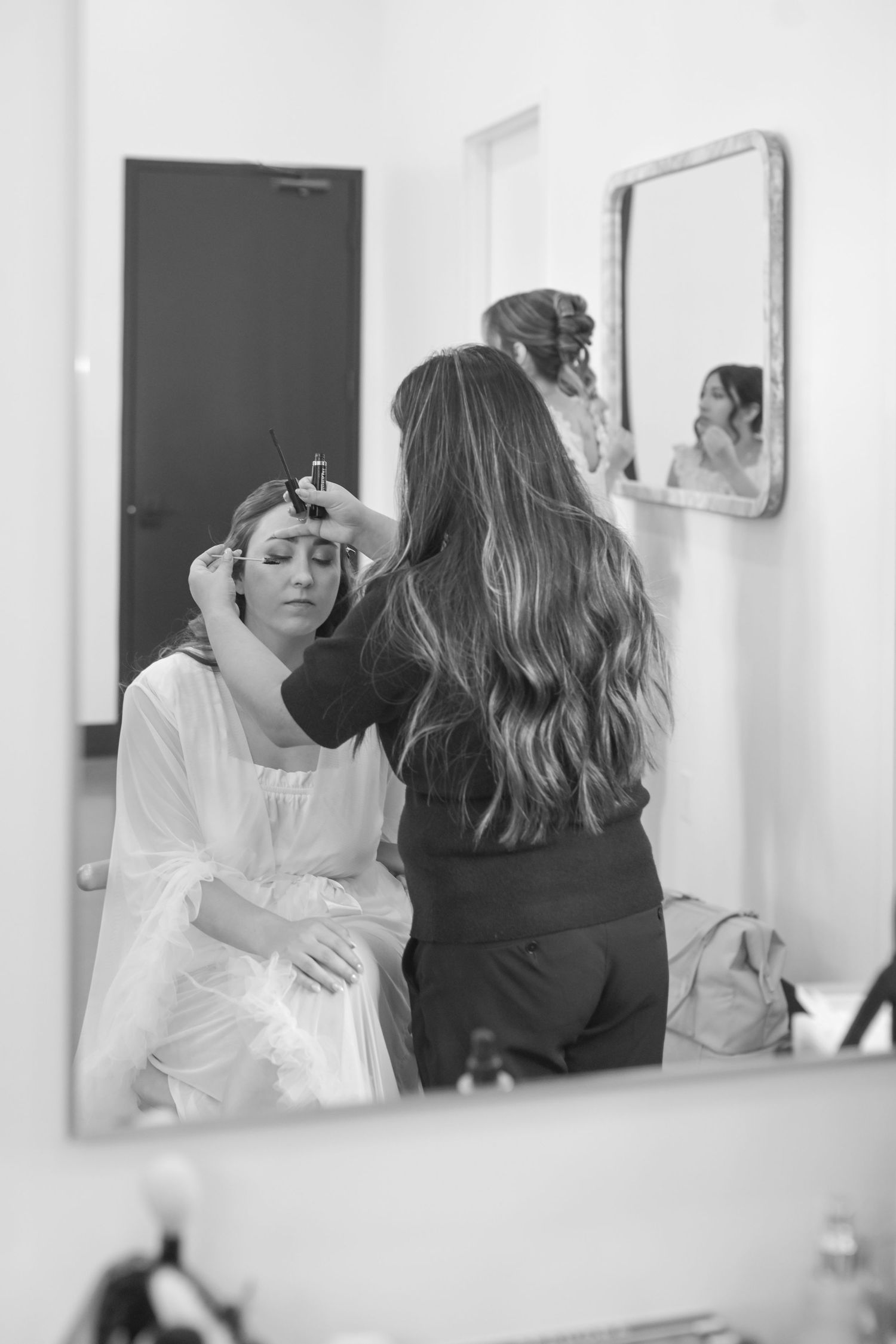 Bride getting hair styled by makeup artist reflected in mirror during wedding preparation.