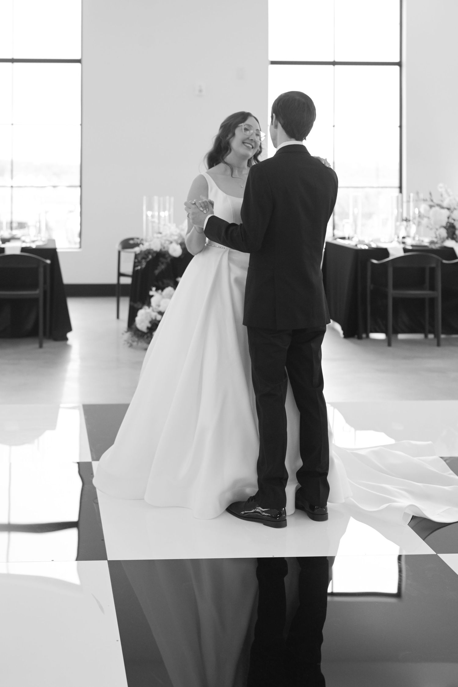 Black and white photo of bride and groom sharing first dance at elegant wedding reception venue.