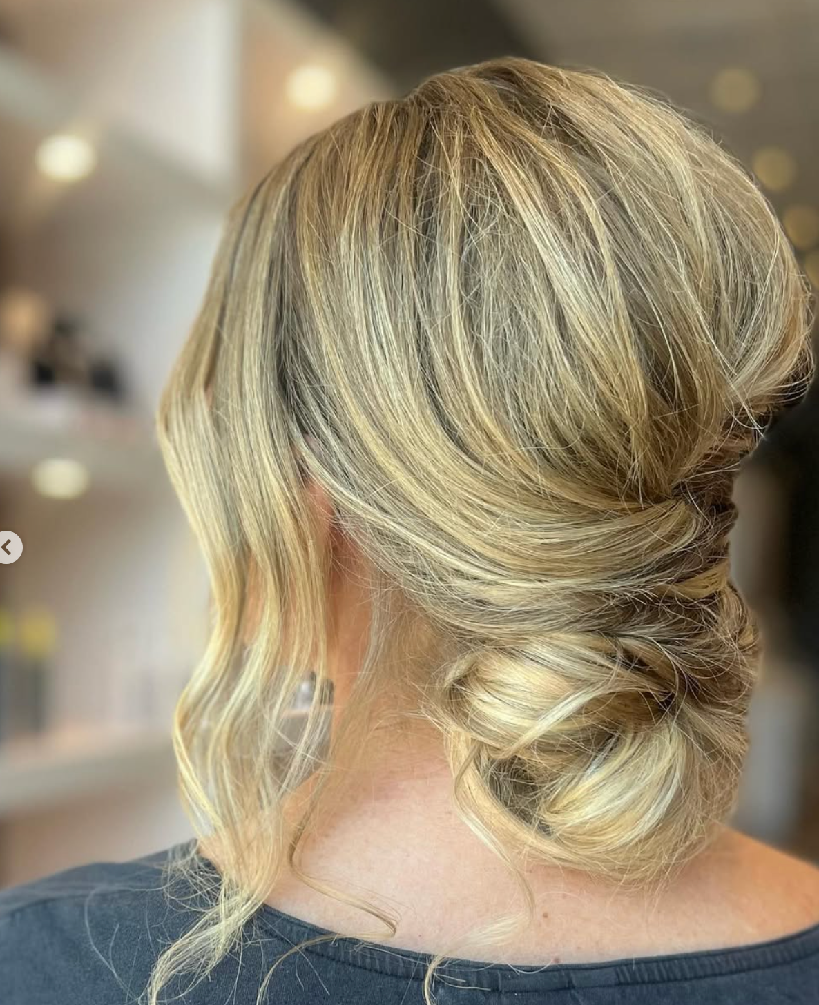 Elegant low bun updo hairstyle with soft blonde highlights and loose face-framing waves, perfect for weddings.