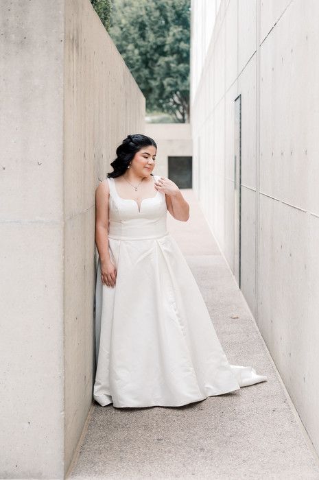 Bride in white A-line gown leaning against concrete wall in narrow passage.
