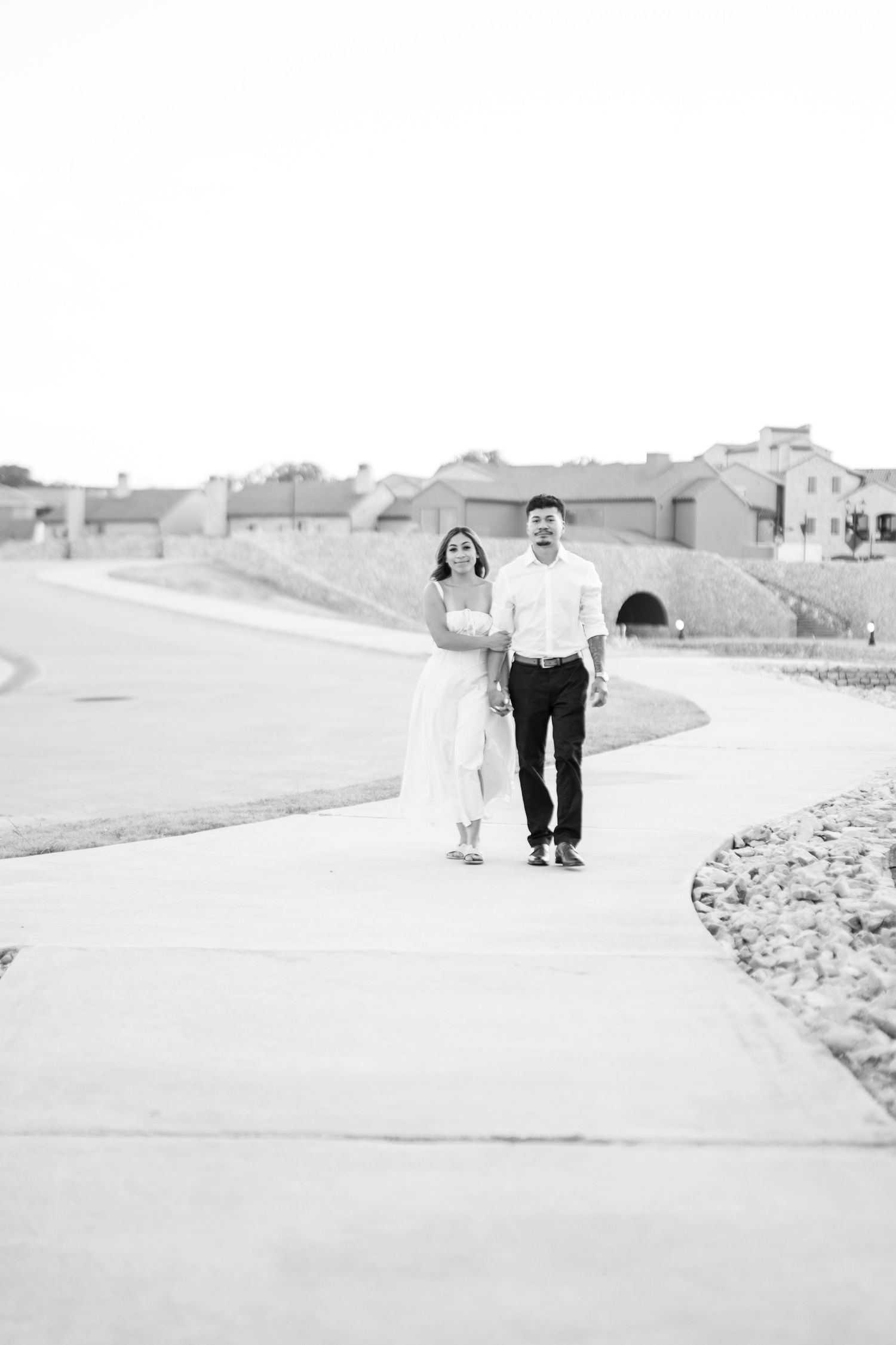 Black and white photo of couple walking together on a sunlit outdoor path.