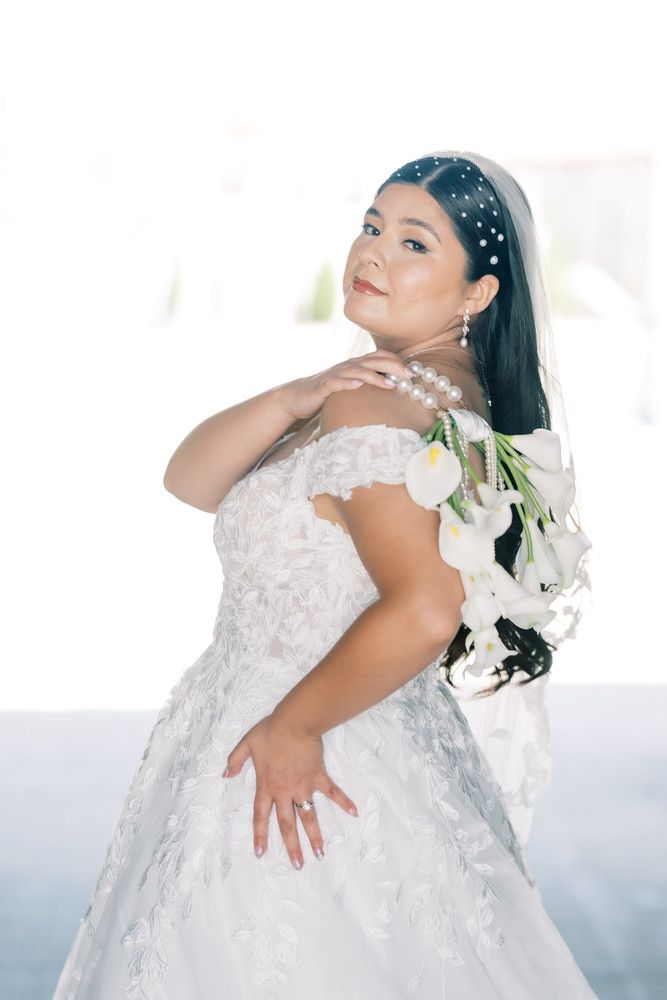 Bride in a detailed lace wedding dress poses with white lilies against a bright background.