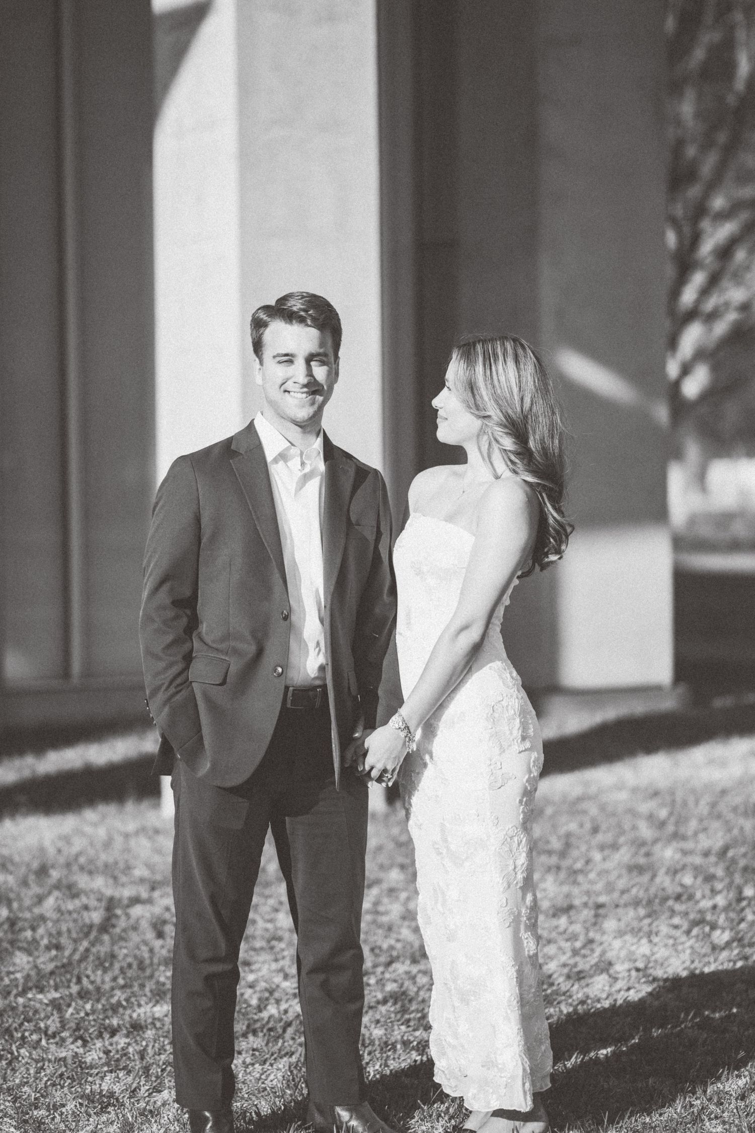 A bride and groom share a romantic moment in black and white as sunlight casts dramatic shadows on a building exterior.