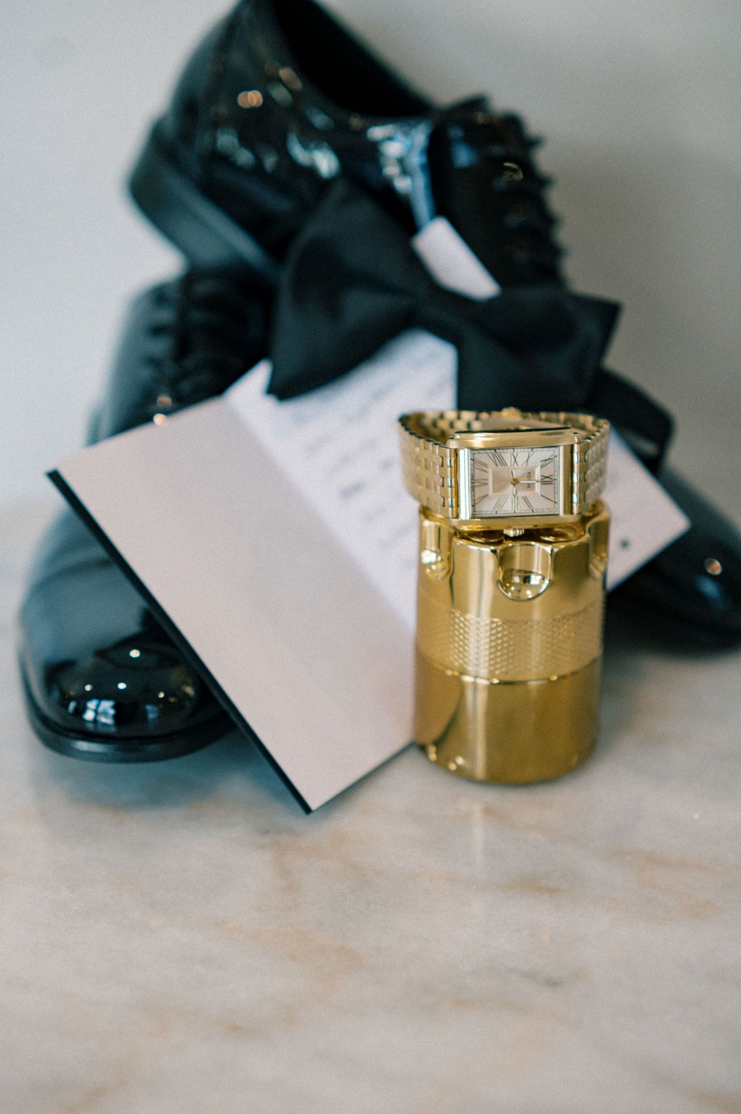 Gold wedding rings and black dress shoes arranged on a light surface.