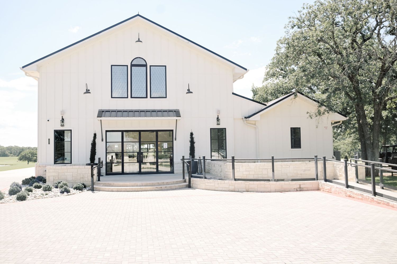 Modern white barn wedding venue with black trim and glass doors on sunny day.