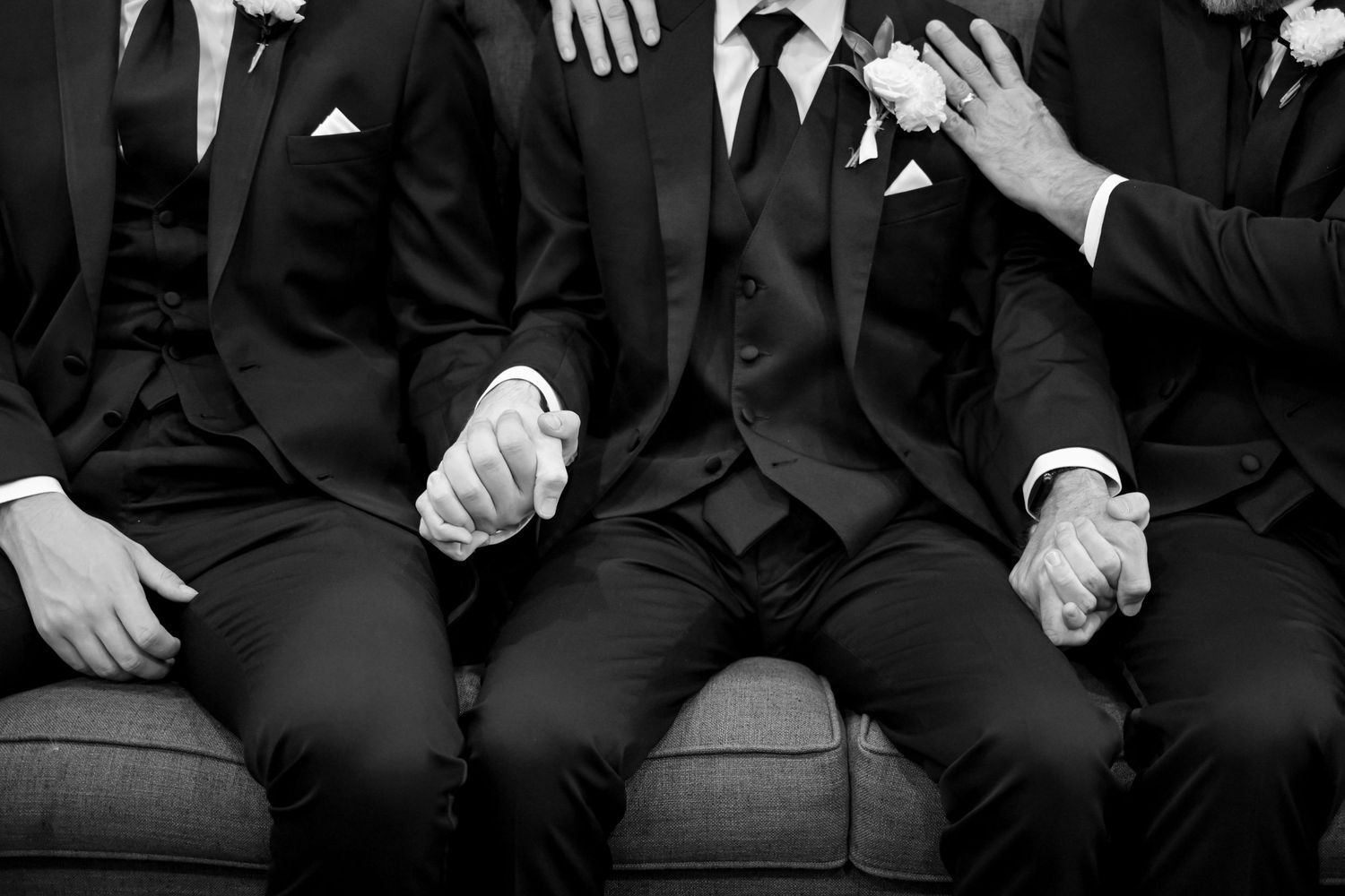 Close-up black and white photo of groomsmen in dark suits seated together at a wedding.
