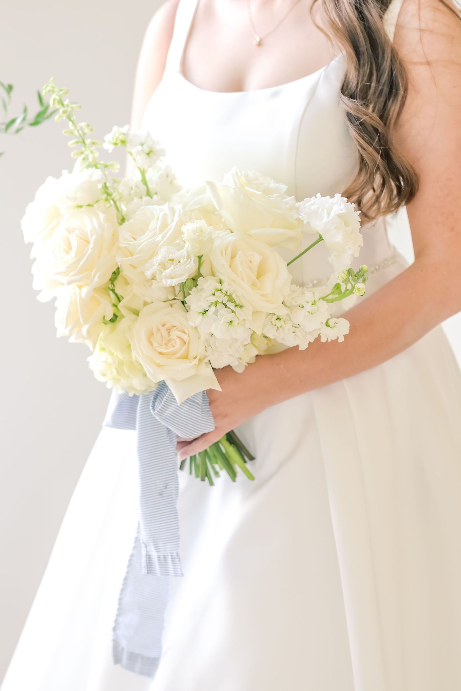 Bride holding an elegant white bouquet of roses and flowers tied with a gray ribbon on her wedding day.
